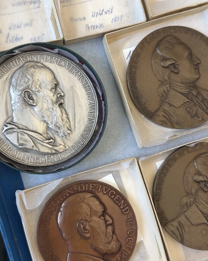 Vier historische Münzen mit Profilportraits verschiedener Männer jeweils in kleinen Kästen