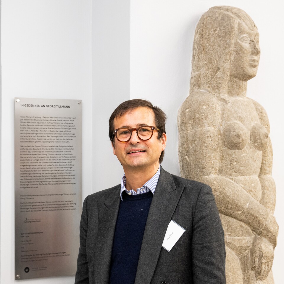 Hugo Tillman, Urenkel von Georg Tillmann vor der Gedenktafel neben einer der beiden Kaminfiguren von Gustav Heinrich Wolff (1986–1934) im Hubertus-Wald-Forum der Hamburger Kunsthalle © Hamburger Kunsthalle, Foto: Romanus Fuhrmann