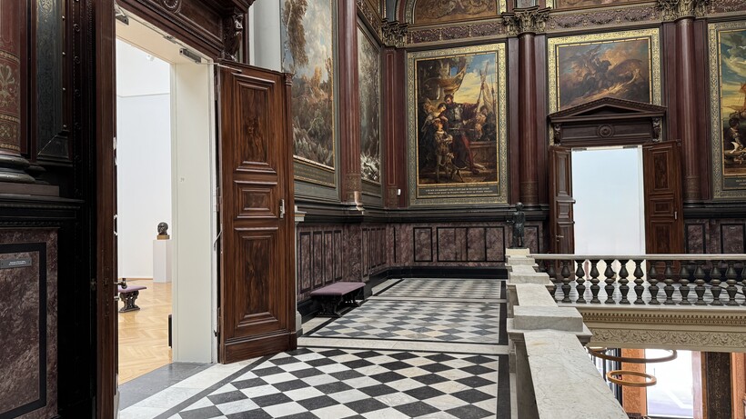 Historischer Innenraum mit schwarz-weißem Schachbrettboden, dunkler Holztäfelung und Gemälden