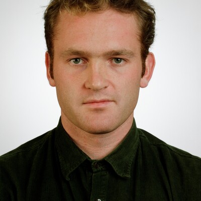 Portraitfoto eines jungen Mannes mit braunem Haar in schwarzem Poloshirt vor weißem Hintergrund